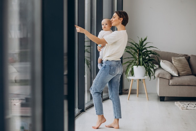 Mère avec bébé debout à la maison près de la fenêtre