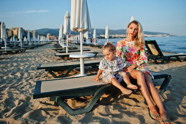 Mère et belle fille s'amusant sur la plage assis sur un lit de bronzage Portrait d'une femme heureuse avec une jolie petite fille en vacances