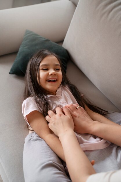 Mère chatouillant un enfant sur un canapé à angle élevé