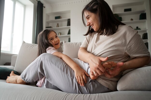 Mère chatouillant enfant sur canapé plein coup