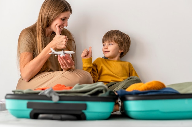 Mère et enfant avec des bagages à la maison donnant les pouces vers le haut