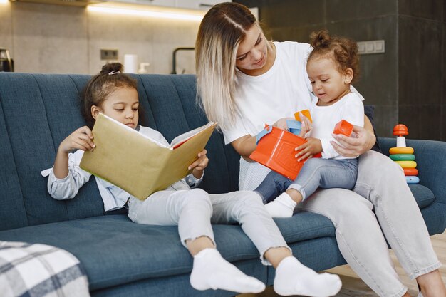 Mère et enfants se détendre ensemble sur le canapé à la maison dans le salon. Les petites filles lisent un livre et jouent à des jouets.