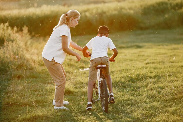 Mère européenne et fils africain. Famille dans un parc d'été. Enfant à vélo.