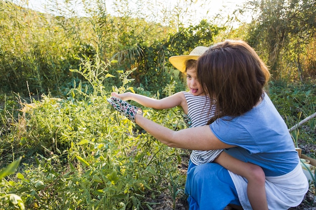 Photo gratuite mère et fille accroupie dans un champ en train de récolter des légumes frais