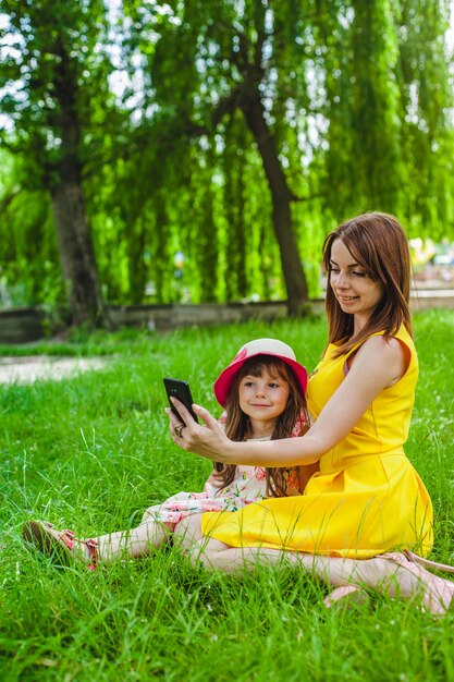 Mère et fille assise sur la pelouse d&#39;un parc regardant un mobile