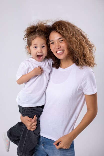 Une mère et une fille bouclées posent sur un fond blanc en chemise blanche.