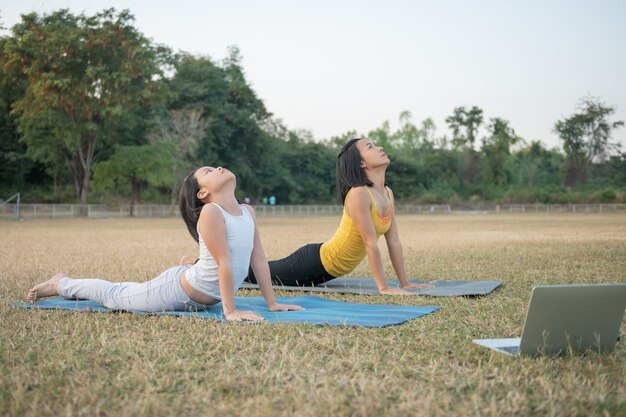 Mère et fille faisant du yoga. femme et enfant s'entraînant dans le parc. sports de plein air. mode de vie sportif sain, regarder des exercices de yoga tutoriel vidéo en ligne et étirer la poitrine et la colonne vertébrale.
