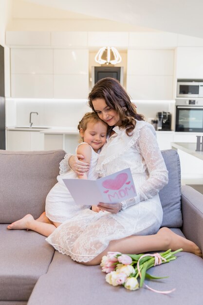 Mère et fille, lecture de carte de voeux ensemble sur le canapé à la maison