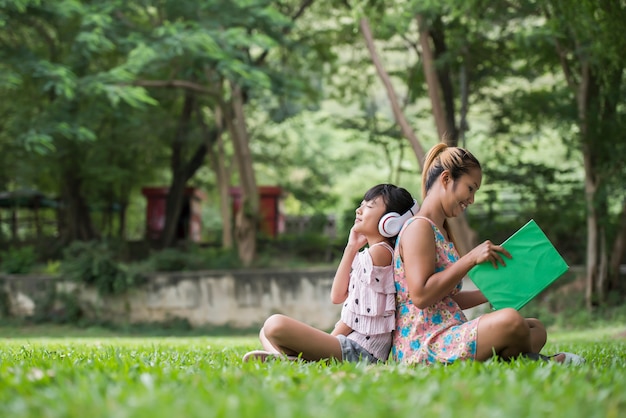 Mère et fille lisant un conte de fées à sa fille écoutent le son avec un casque dans le parc