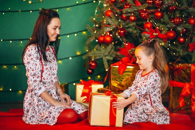 Mère avec fille par sapin de Noël déballant des cadeaux