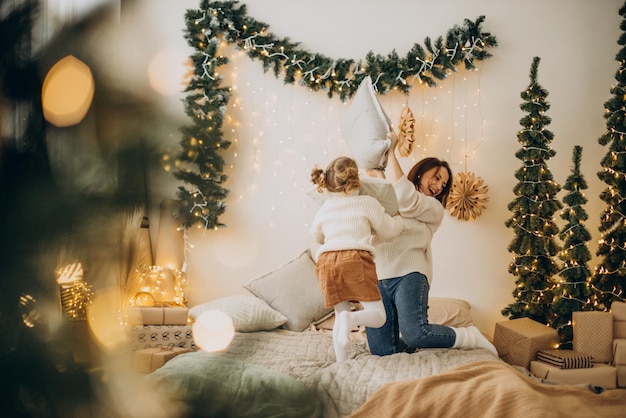 Mère avec fille s'amusant avec des oreillers sur le lit à Noël