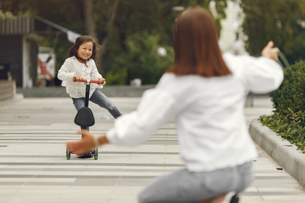 Mère et fille sur le scooter de coup dans le parc. Les enfants apprennent à faire du skateboard. Petite fille patinant sur une journée d'été ensoleillée.