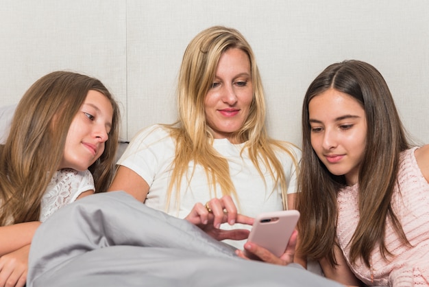 Mère Et Filles Assises Avec Smartphone Au Lit