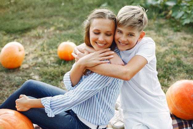 Photo gratuite mère et fils assis sur un jardin près de nombreuses citrouilles