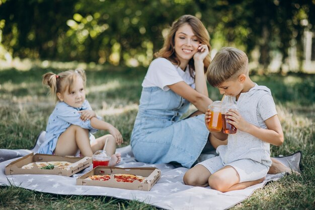 Mère avec fils et fille mangeant de la pizza dans le parc