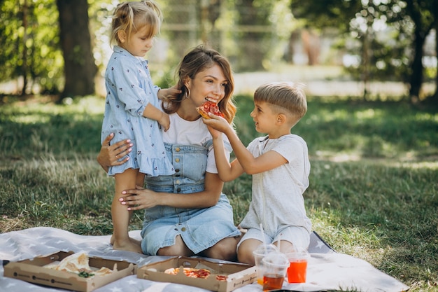 Mère avec fils et fille mangeant de la pizza dans le parc