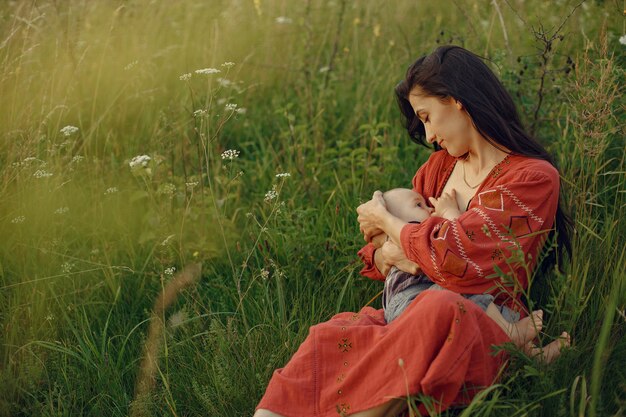 Mère avec jolie fille. Maman allaite son petit fils. Femme en robe rouge.