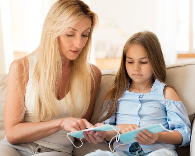 Mère montrant à sa fille comment porter des masques médicaux