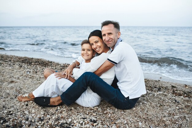 Mère, père et fils est assis sur la plage près de la mer, étreignant et regardant droit