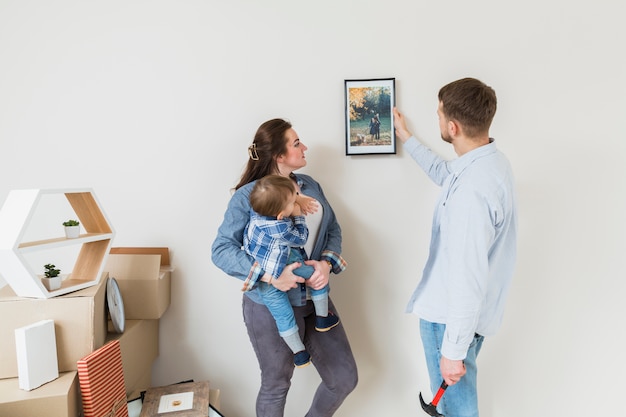 Mère portant son fils en regardant cadre attaché par son mari sur le mur