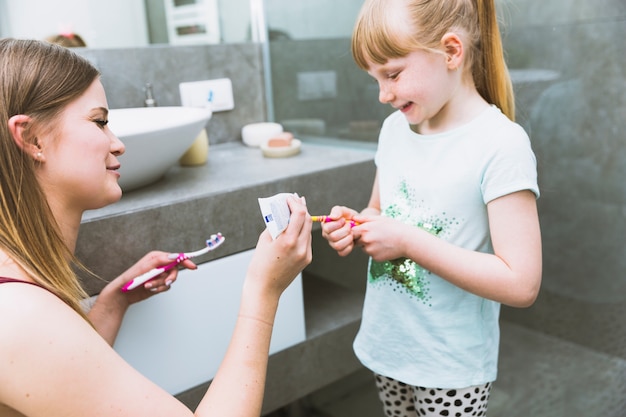 Mère serrant la pâte sur la brosse à dents de la fille