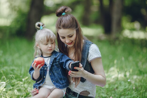 Mère souriant tandis que sa fille mange une pomme et en jouant avec le mobile