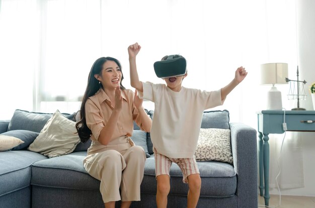 Mère souriante regardant son fils jouer à des jeux en utilisant un casque de réalité virtuelle VR à la maison Concept futur de la technologie