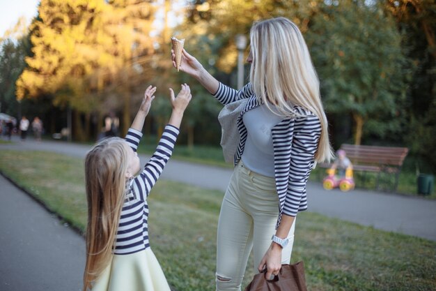 Mère tenant un cornet de crème glacée pendant que sa fille essaie de le ramasser