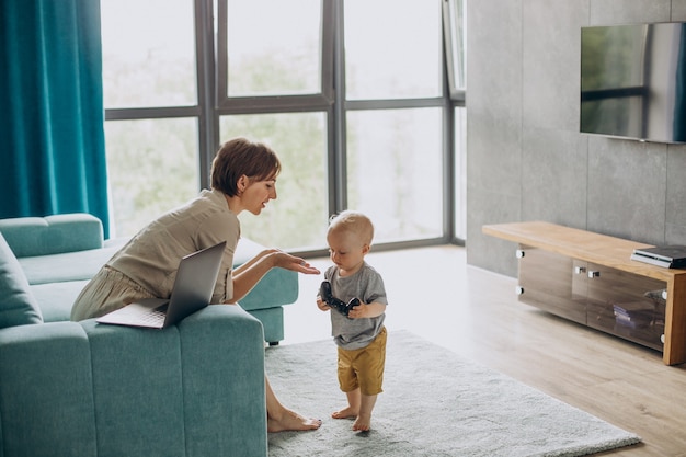 Mère Travaillant Sur Un Ordinateur Portable Pendant Que Son Fils Joue à Des Jeux Vidéo