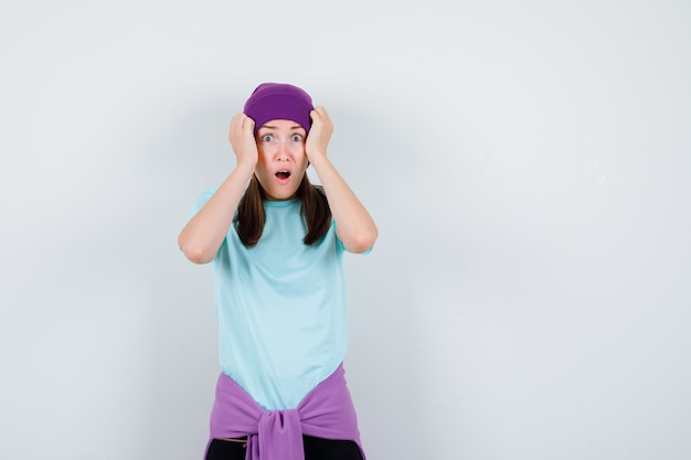 Merveilleuse dame en chemisier, bonnet avec les mains sur la tête et l'air horrifié, vue de face.