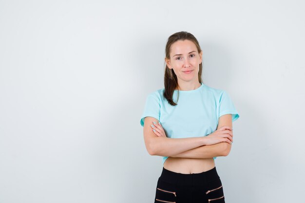 Merveilleuse femme en chemisier, pantalon avec les mains croisées et l'air confiant, vue de face.