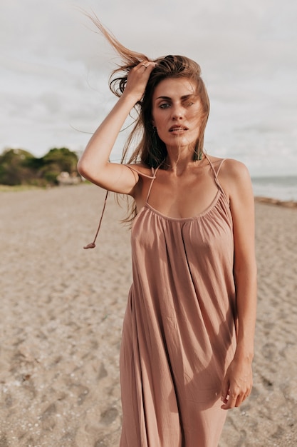 Merveilleuse femme élégante aux cheveux longs portant une robe longue posant en marchant sur la plage