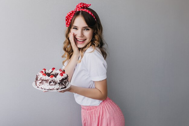 Merveilleuse fille d'anniversaire exprimant des émotions sincères positives. Tir intérieur d'une dame européenne heureuse en tenue vintage posant avec un gâteau sucré.