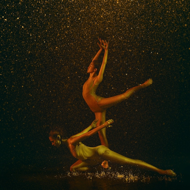 Merveilleux. Deux jeunes danseuses de ballet sous des gouttes d'eau et de pulvérisation. Modèles caucasiens et asiatiques dansant ensemble dans des néons. Ballet et concept de chorégraphie contemporaine. Photo d'art créatif.