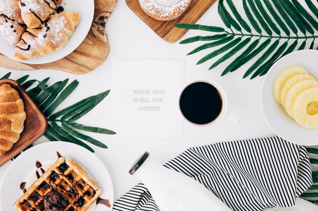 Message sur le bloc-notes entouré d&#39;un petit-déjeuner cuit au four; tranches de café et d&#39;ananas sur un bureau blanc