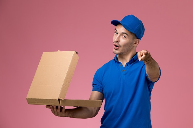 Messager mâle en uniforme bleu tenant la boîte de livraison de nourriture en l'ouvrant sur rose, la prestation de services uniforme des travailleurs