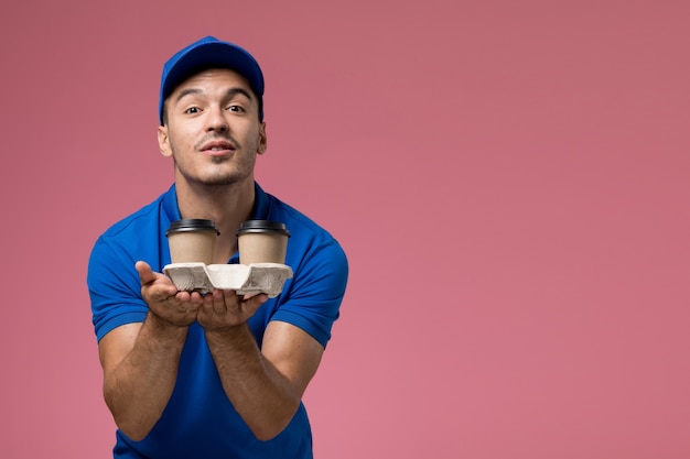 Photo gratuite messager masculin en uniforme bleu offrant des tasses à café sur rose, travailleur de la prestation de services uniforme