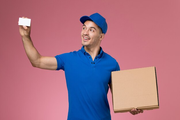Messager masculin en uniforme bleu tenant la boîte de nourriture et la carte avec le sourire sur le rose, la prestation de services uniforme des travailleurs