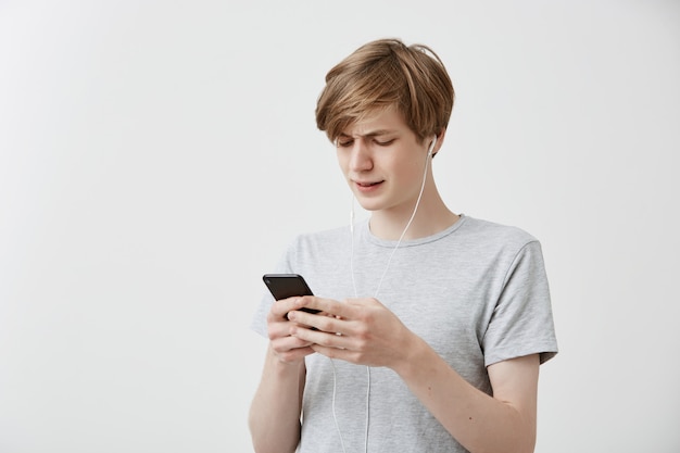 Messages de gars hipster perplexes choqués avec des amis, utilise une connexion Internet gratuite sur un téléphone portable moderne, reçoit de mauvaises nouvelles. Un jeune homme étonné reçoit de mauvaises nouvelles. Sentiments humains, émotions, réaction