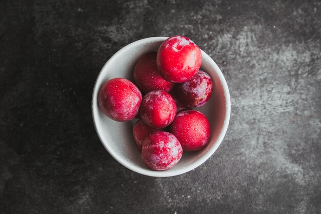 Mettre les prunes à plat dans un bol sur fond noir texturé.