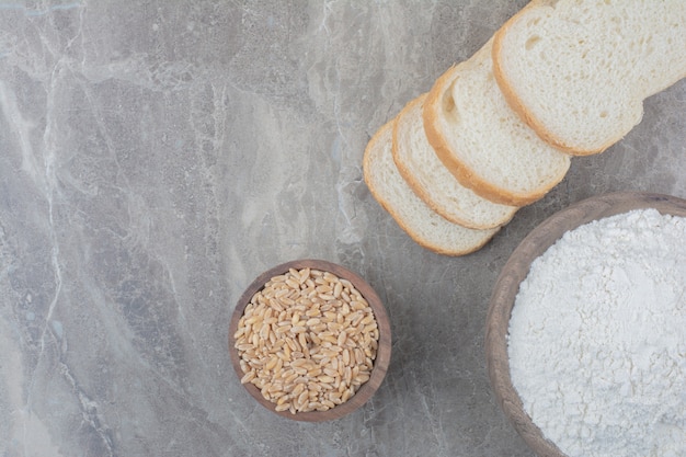 Une miche de pain blanc avec des grains d'avoine et de la farine sur fond de marbre.