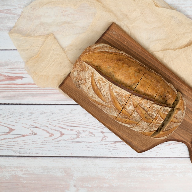 Photo gratuite miche de pain avec des tranches sur une planche à découper et une nappe sur le bureau en bois