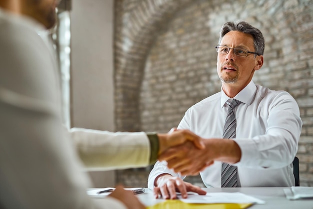 Mid adult manager serrant la main d'un candidat lors d'un entretien d'embauche au bureau