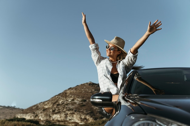 Mid shot femme blonde hors de la fenêtre de la voiture avec les mains en l'air