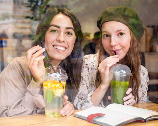 Photo gratuite mid shot femmes buvant des jus de fruits frais au café