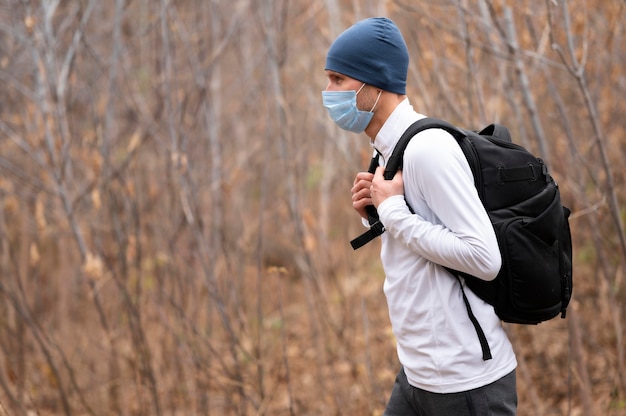 Mid shot male avec masque facial et sac à dos dans les bois