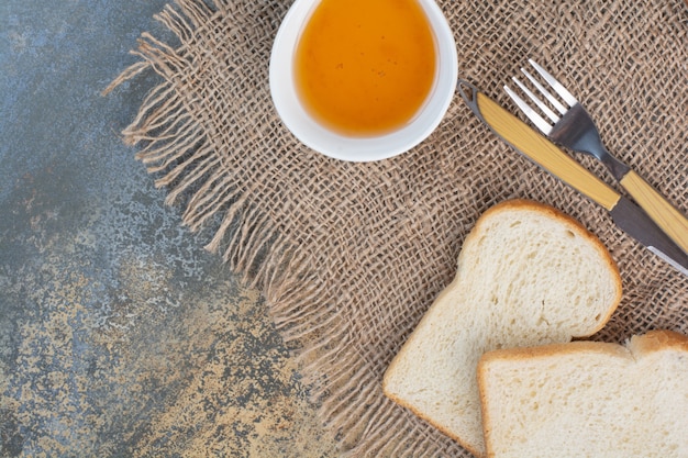 Miel, tranches de pain et couverts sur toile de jute.