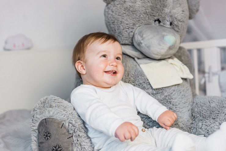 Photo gratuit un mignon bébé blond dans un lit blanc avec un ours en peluche