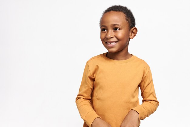 Mignon écolier afro-américain en sweat-shirt jaune posant contre un mur blanc avec copie espace pour votre information