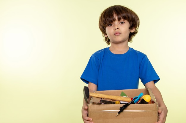 Photo gratuite mignon garçon en bleu t-shirt tenant la boîte avec des outils sur le mur blanc